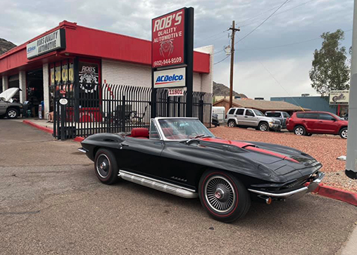 Black classic Corvette convertible with red stripe in front of the shop